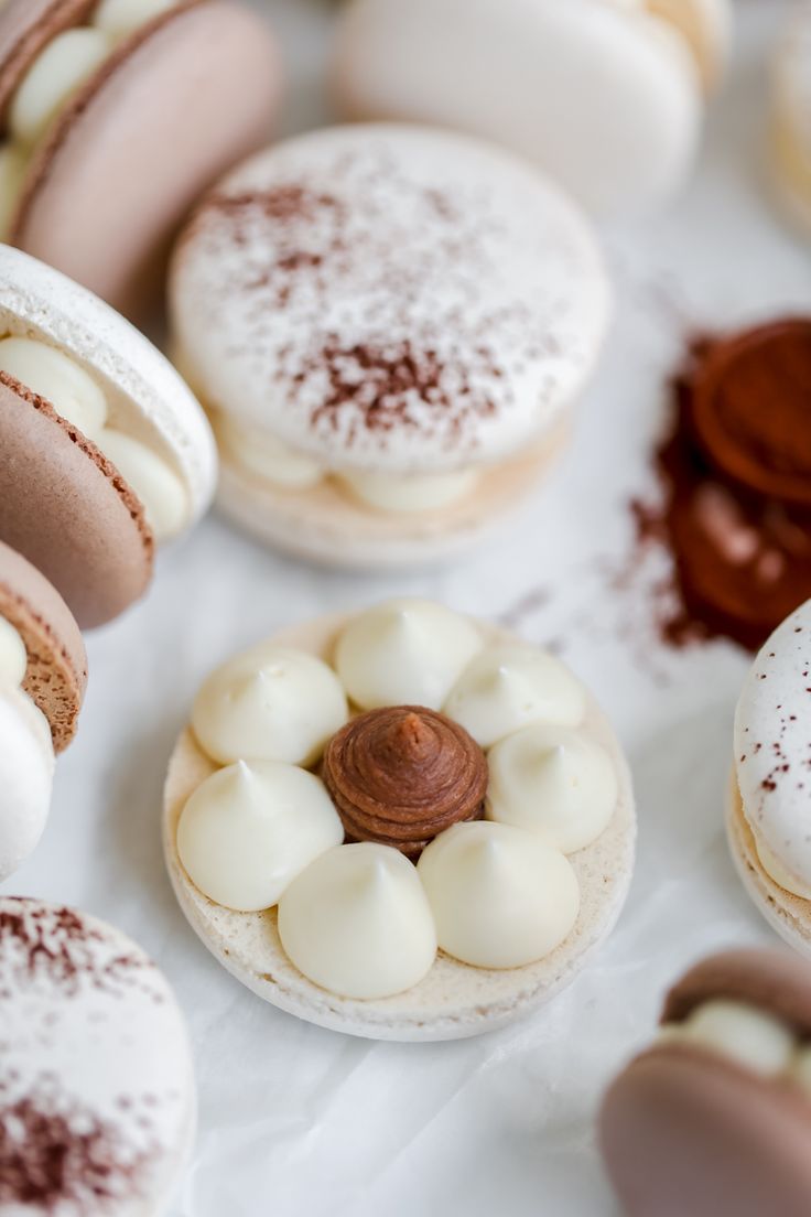 many different types of macaroons are on the white tablecloth with brown and white icing