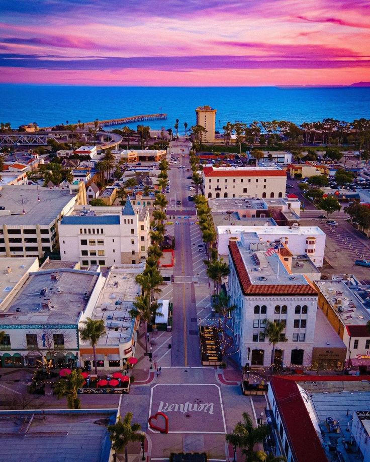 an aerial view of a city with buildings and the ocean in the background at sunset