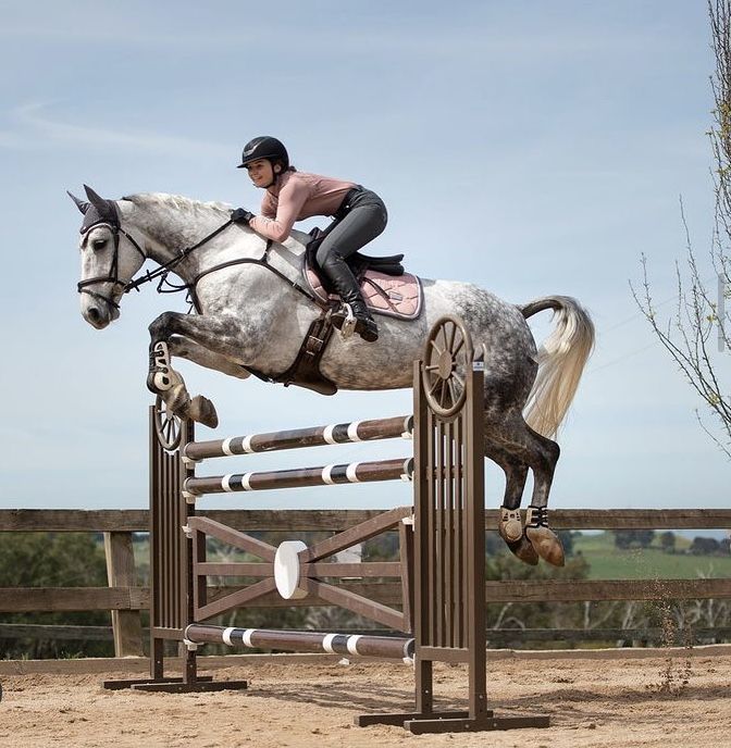 a woman riding on the back of a white horse over an obstacle with her legs in the air