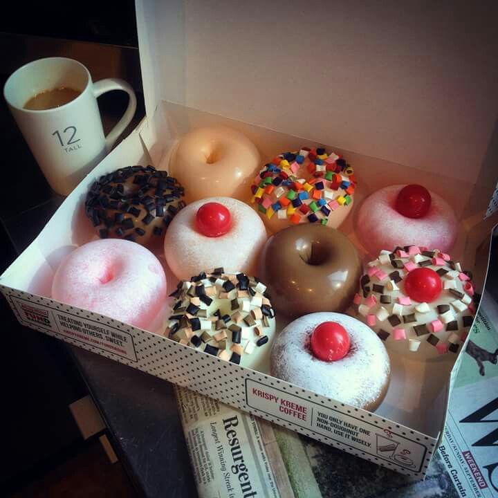 a box filled with lots of different flavored donuts next to a cup of coffee