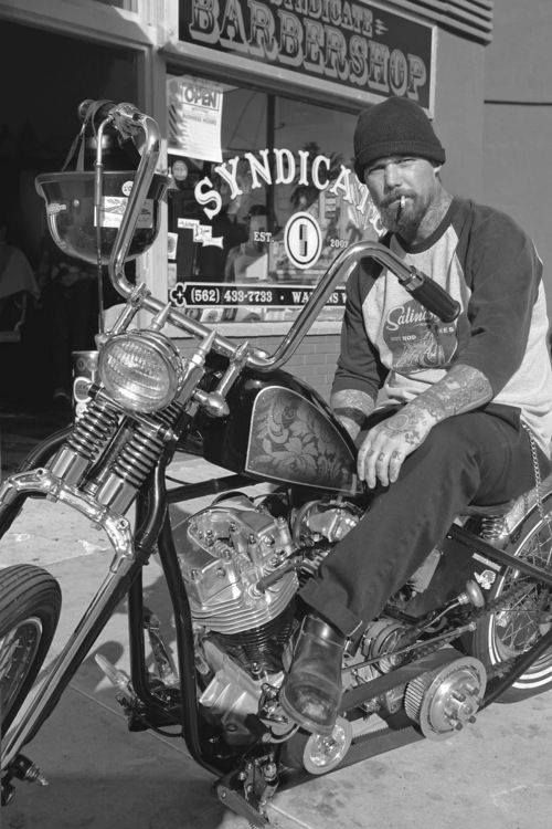 a man sitting on top of a motorcycle in front of a barbershop and salon