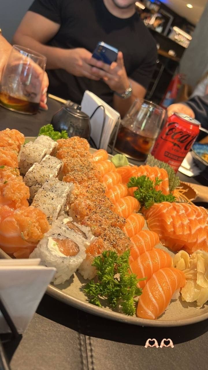 a plate full of sushi and other food on a table with people in the background