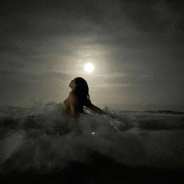 a woman sitting in the ocean at night with her eyes closed and head turned to the side