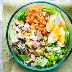 a glass bowl filled with meat, vegetables and hard boiled eggs on top of a green cloth