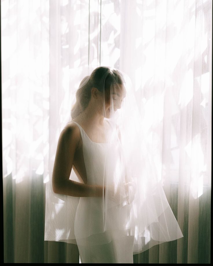 a woman standing in front of a window wearing a white dress and holding her hands on her hips