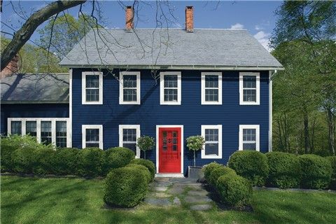 a blue house with white trim and red door in the middle of a green yard