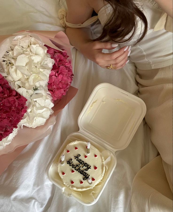 a woman laying in bed next to a cake and flower box with the word happy birthday written on it