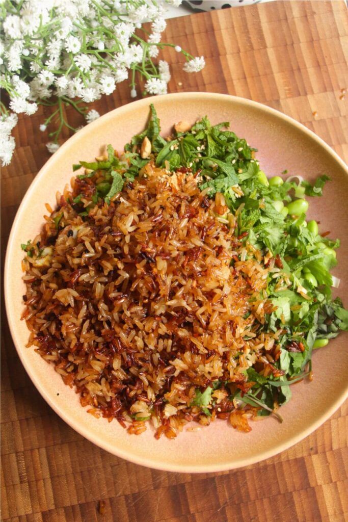 a bowl filled with rice and greens on top of a wooden table next to flowers