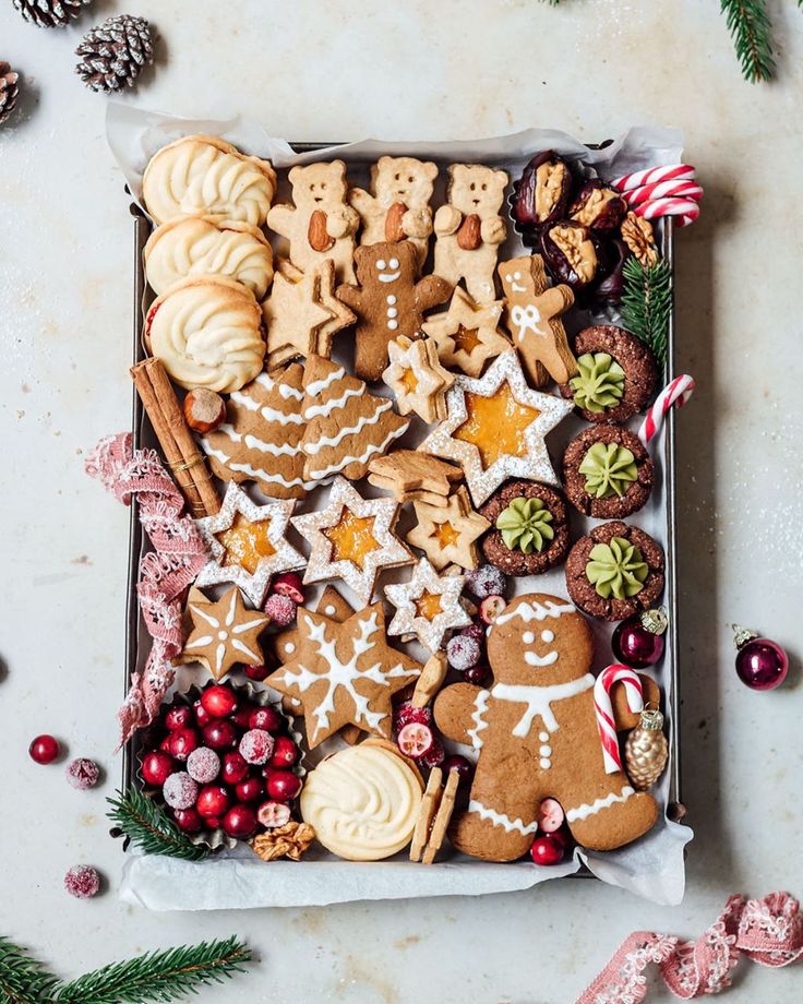 two hands reaching for christmas cookies in a box surrounded by other holiday foods and decorations