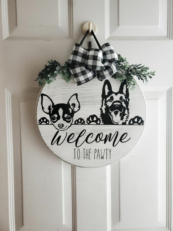 a welcome sign hanging on the front door with two dogs in black and white checkered bow