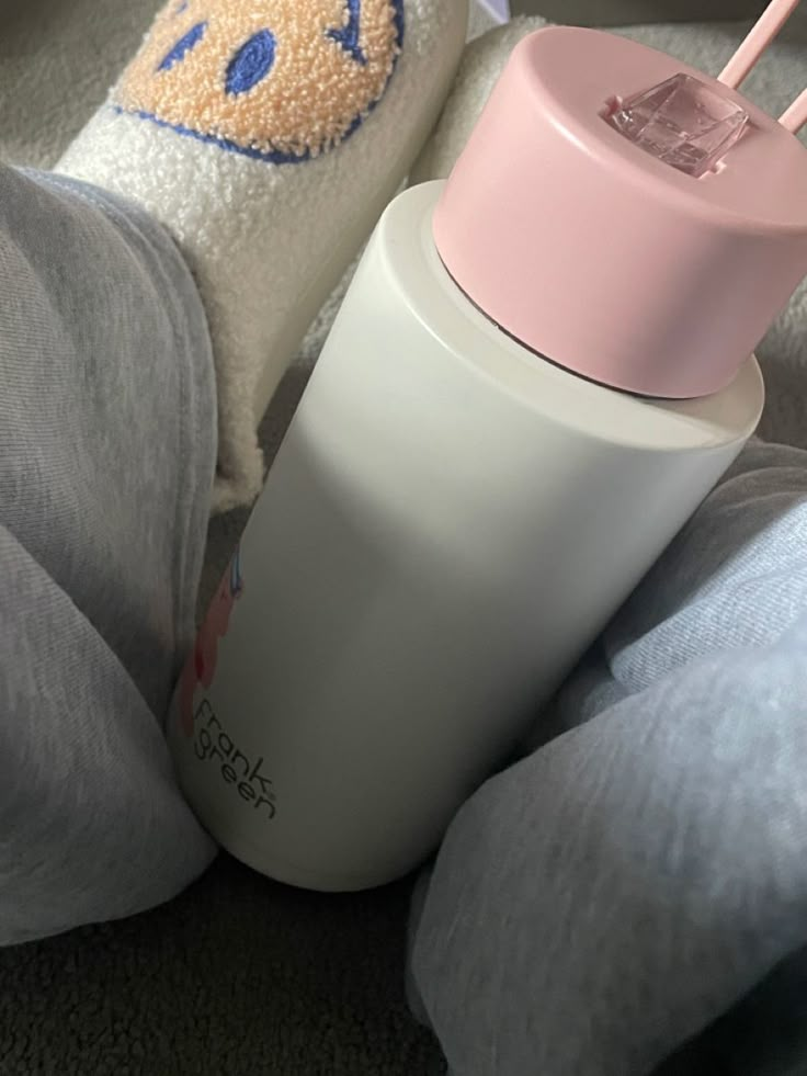 a pink and white baby bottle sitting on top of a bed next to a stuffed animal