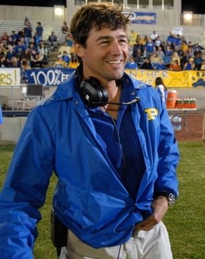 a man with headphones on standing in front of a crowd at a football game