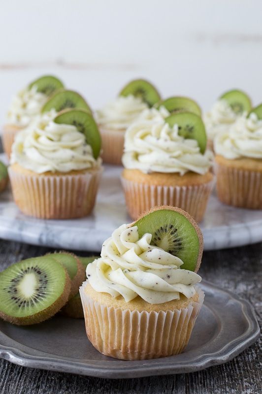 cupcakes with kiwi slices and whipped cream frosting on a silver plate