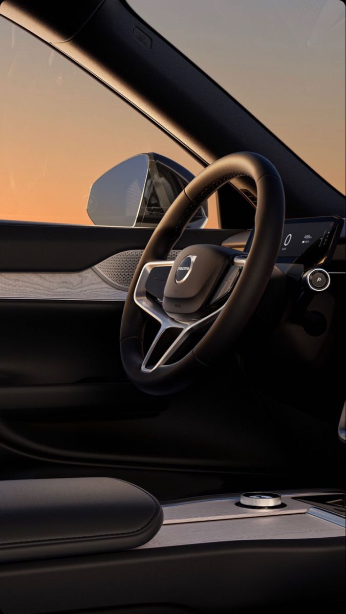 the interior of a modern car with steering wheel and dashboard, in front of an orange sky