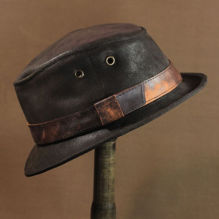 As fans of vintage hats, we are constantly looking for interesting natural leather with an aged effect. So this time we managed to get something special for you. Leather trilby hat TRL-22 is a new item in our catalog, which we can rightfully be proud of. Dense but soft dark brown leather is reminiscent of the good old days when wearing a hat was commonplace. The crown of the hat has 6 mm eyelets on the sides for ventilation. 25 mm leather band with same leather loop. Cotton lining. Crown height - 85/95 mm. The brim width - 45/50 mm. Black Leather Vintage Hat, Brown Brimmed Hats With Leather Sweatband, Vintage Black Leather Hat Bands, Retro Brown Leather Hat, Vintage Leather Fedora Hat Band, Vintage Adjustable Leather Hat Bands, Adjustable Leather Vintage Hat Bands, Brown Hats With Leather Lining And Curved Brim, Brown Curved Brim Hat With Leather Lining