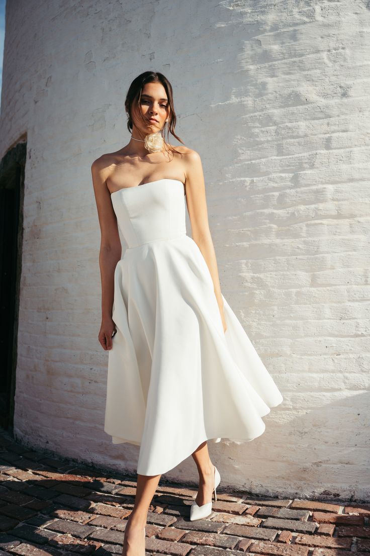 a woman wearing a white dress and high heels standing in front of a brick wall