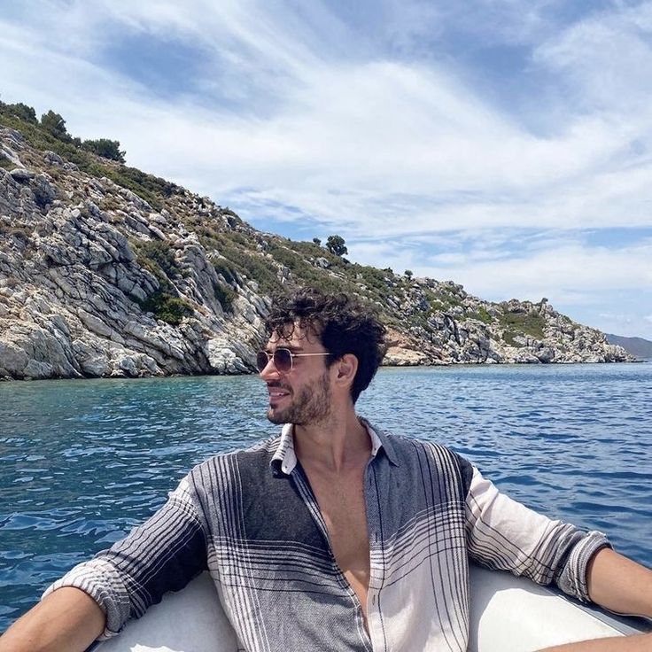 a man sitting on top of a boat in the ocean next to a rocky shore