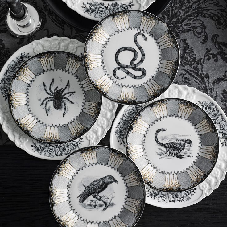 four black and white plates with gold designs on them, one has a spider in the middle