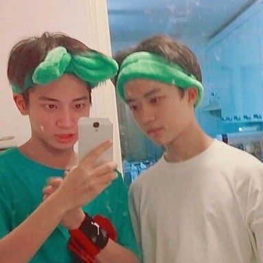 two young men wearing green hair ties while looking at a cell phone