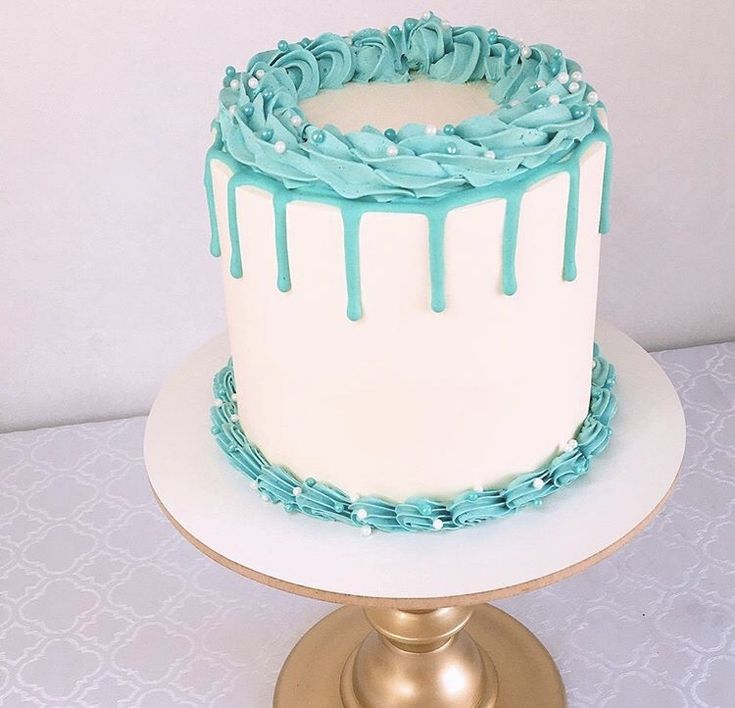 a white cake with blue icing sitting on top of a gold plated stand