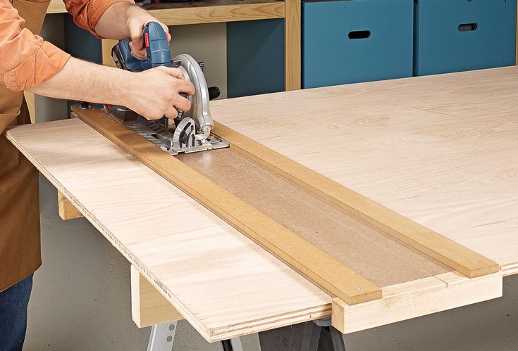 a person using a circular saw to cut plywood planks on a workbench