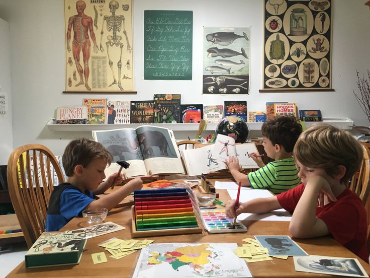 three children sitting at a table with books and pencils in front of them,