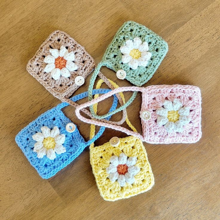 four crocheted square purses with flowers on them sitting on a wooden surface