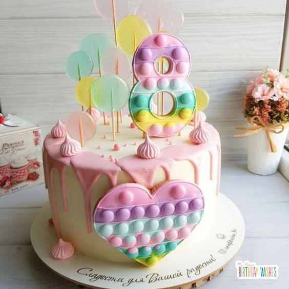 a birthday cake decorated with pink, yellow and blue icing on a white table