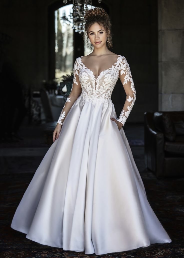 a woman in a white wedding dress standing under a chandelier with her hands on her hips