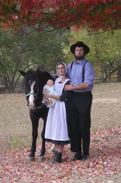 a man, woman and child standing next to a horse in a field with leaves on the ground