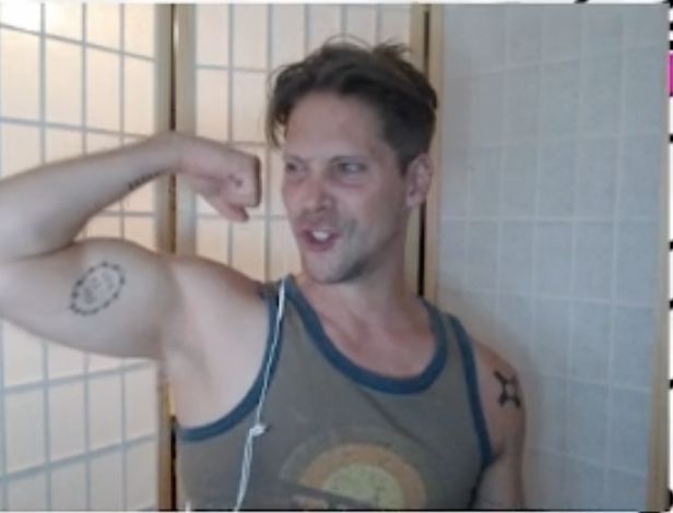 a man in grey tank top standing next to tiled wall and holding his arm up