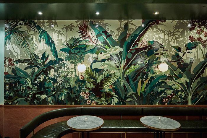 the wall is decorated with tropical plants and foliage, along with two round tables in front of it