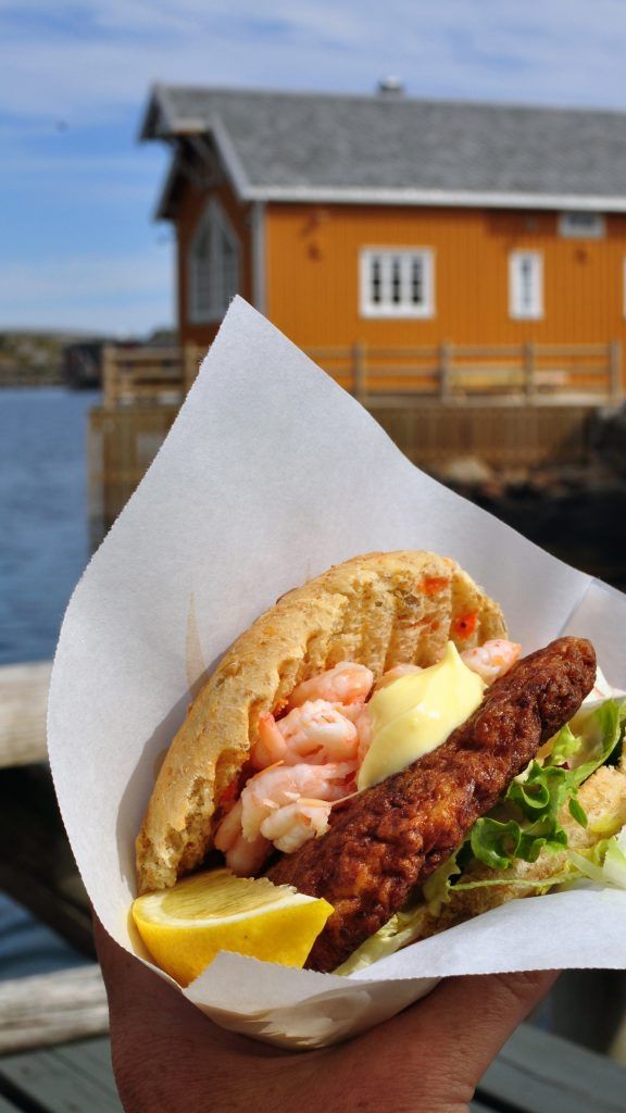 a person holding a sandwich with shrimp, lettuce and lemon wedges in their hand