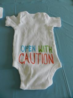 an open with caution sign on a baby's white bodysuit sitting on a blue sheet