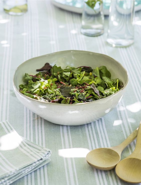 a white bowl filled with green salad on top of a blue and white table cloth