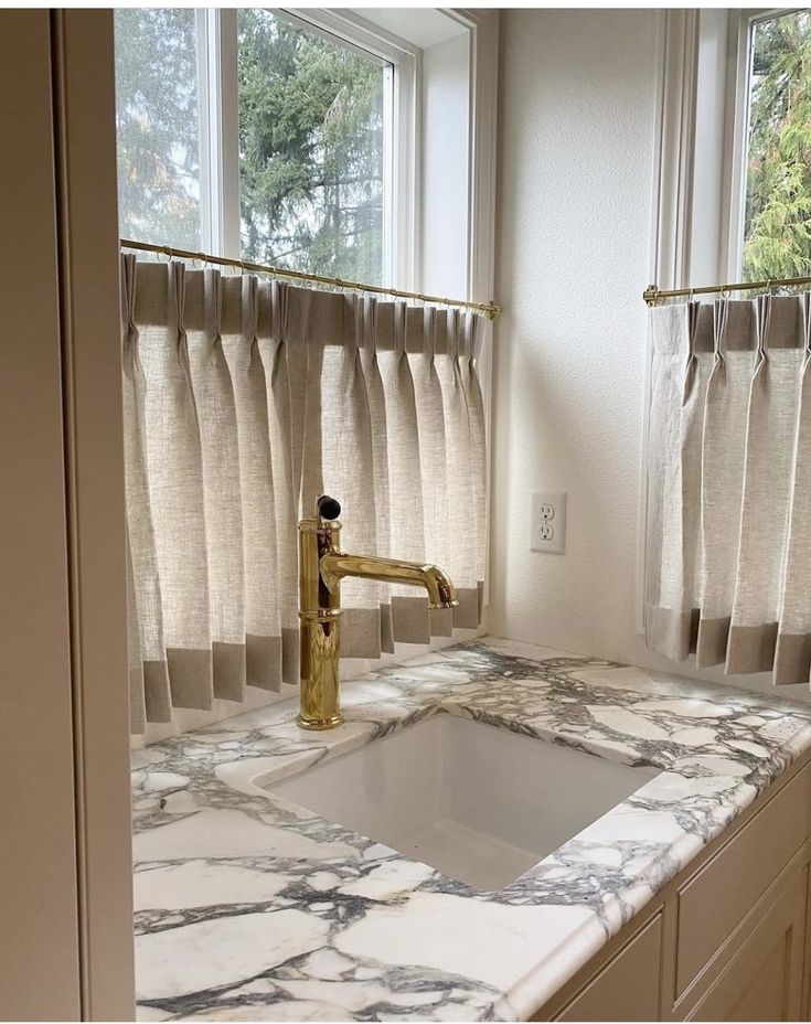 a kitchen with marble counter tops and gold faucet in front of the window