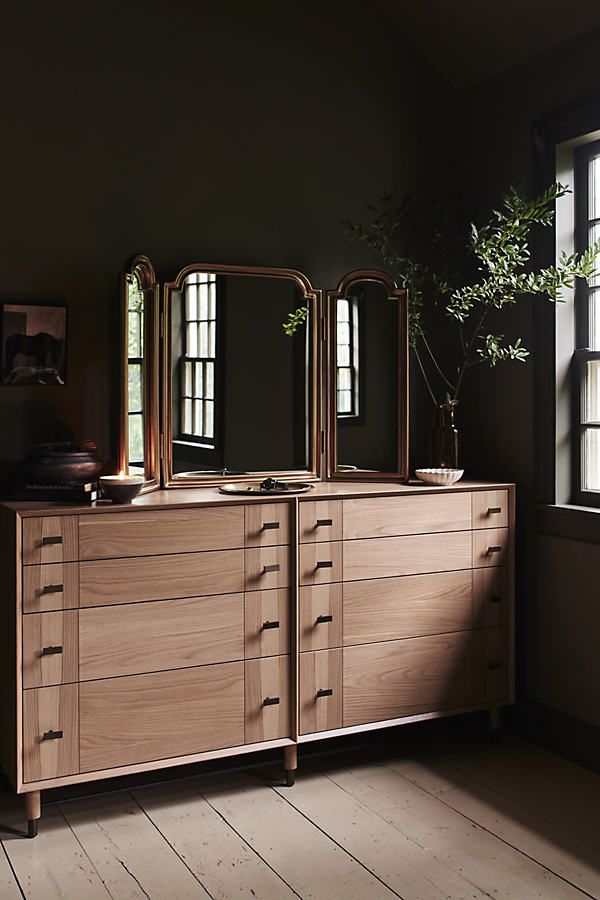 a large wooden dresser sitting next to a window with two mirrors on top of it