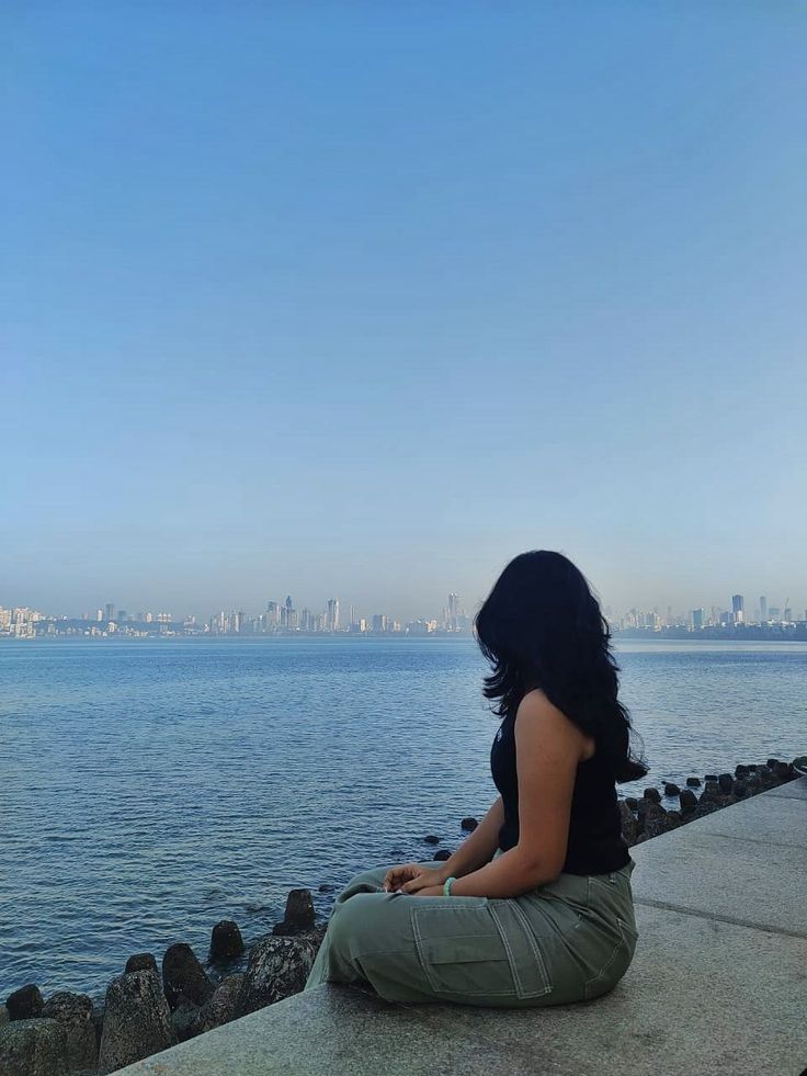 a woman sitting on the edge of a pier looking at the water