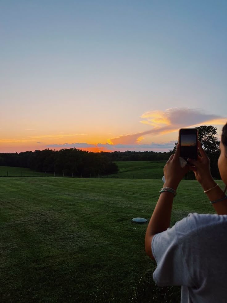 a person is taking a photo with their cell phone in the field at sunset or dawn