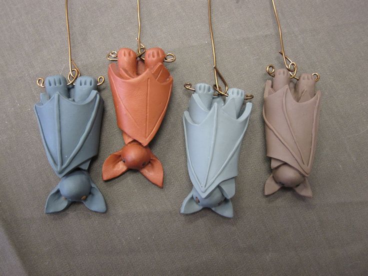 four different colored clay fish ornaments hanging from gold chains on a gray cloth covered surface