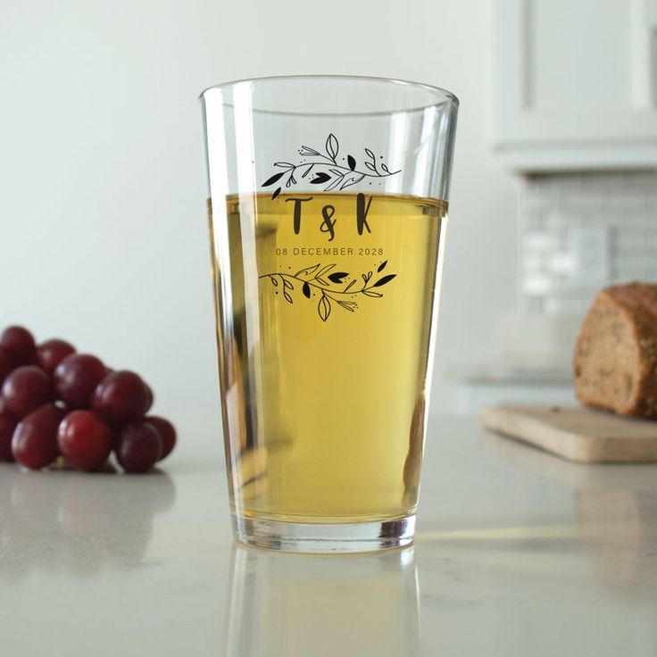 a glass filled with liquid sitting on top of a counter next to grapes and bread