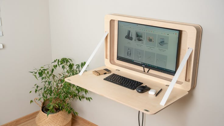 a computer monitor sitting on top of a wooden desk next to a potted plant