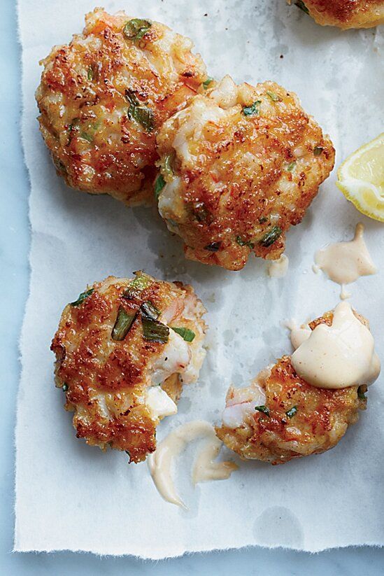 three crab cakes on wax paper with lemon wedges and mayonnaise drizzled around them