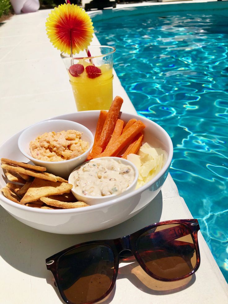 a bowl of food next to a pool with sunglasses on the side and a drink