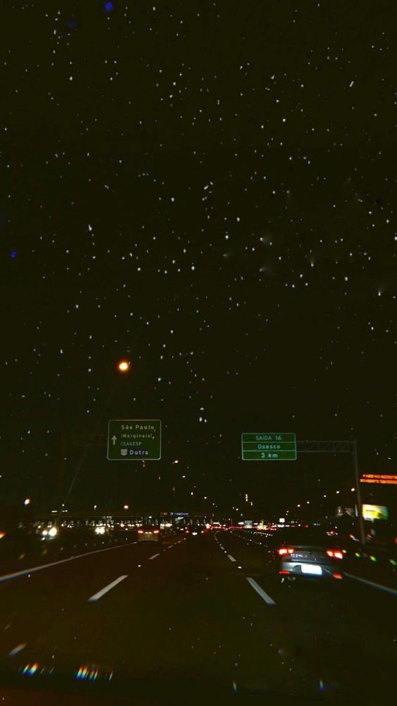 the night sky is filled with stars and street signs as cars drive down the road