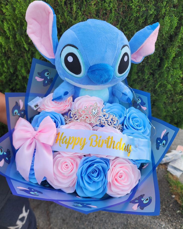 a blue stuffed animal with pink roses in it's lap that says happy birthday