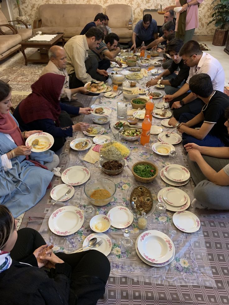 a group of people sitting at a long table eating food from bowls and plates on it