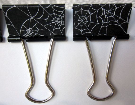 three black and white paper clips with spider web designs on them, hanging from hooks