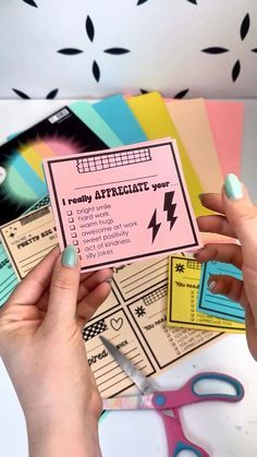 a woman holding up a pink and black card with some scissors next to it on top of a table