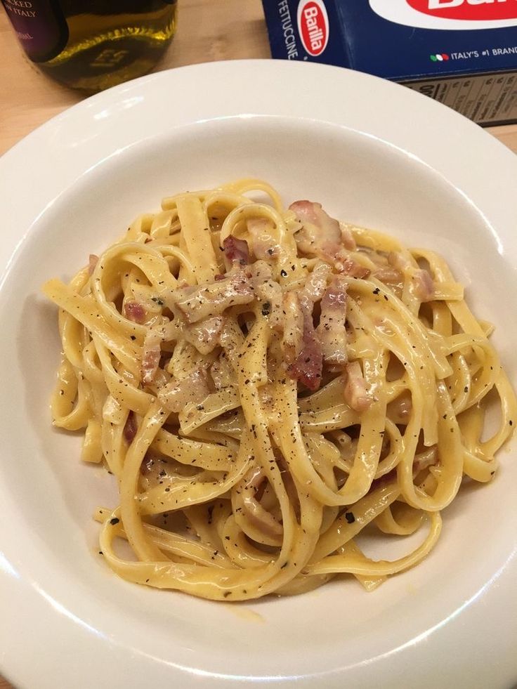 a white plate topped with pasta covered in meat and sauce next to a bottle of wine